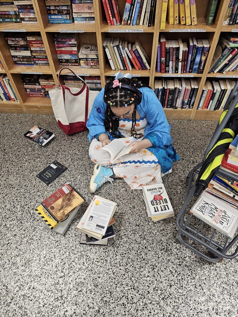 Alora reading on a bookstore floor surrounded by books